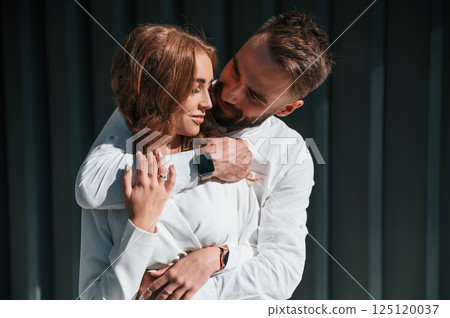 Embracing each other. Beautiful young couple is standing together against dark green background 125120037