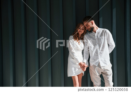 Beautiful young couple is standing together against dark green background 125120038