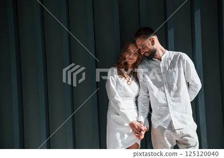 Beautiful young couple is standing together against dark green background Beautiful young couple is standing together against dark green background 125120040