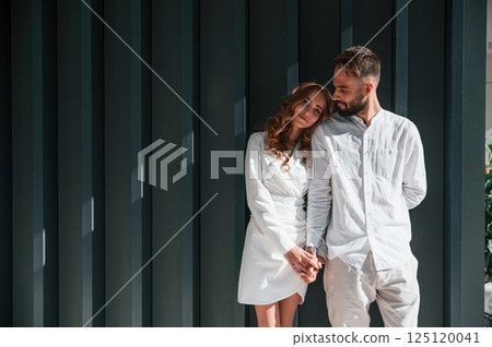 Standing and holding each other by hands. Beautiful young couple is standing together against dark green background 125120041