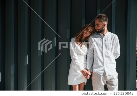 Standing and holding each other by hands. Beautiful young couple is standing together against dark green background Standing and holding each other by hands. Beautiful young couple is standing together against dark green background 125120042