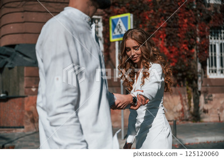 Having fun and holding each other by hands. Beautiful young couple is together on the street against old building 125120060