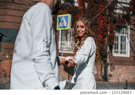 Having fun and holding each other by hands. Beautiful young couple is together on the street against old building Having fun and holding each other by hands. Beautiful young couple is together on the street against old building 125120061