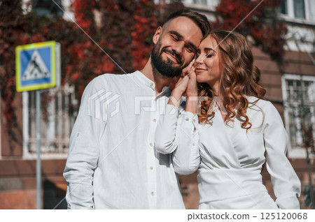 Standing and embracing each other. Beautiful young couple is together on the street against old building 125120068