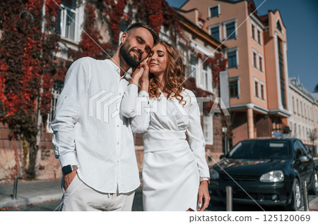 Standing and embracing each other. Beautiful young couple is together on the street against old building 125120069