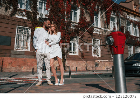 Standing and embracing each other. Beautiful young couple is together on the street against old building 125120072
