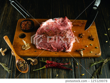 A generous cut of raw beef is placed on a wooden cutting board, surrounded by an array of spices. The rich marbling of the meat is highlighted as it awaits seasoning for a delicious meal A generous cut of raw beef is placed on a wooden cutting board, surrounded by an array of spices. The rich marbling of the meat is highlighted as it awaits seasoning for a delicious meal 125120078