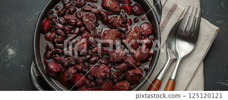 Brazilian feijoada with black beans, sausage and meat in a pot, top view 125120121