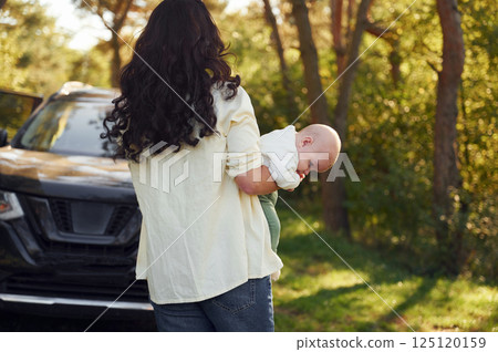 Baby is on the hands. Beautiful mother with her little son is outdoors in the forest Baby is on the hands. Beautiful mother with her little son is outdoors in the forest 125120159