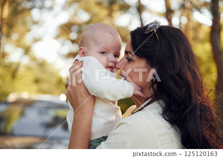 Holding her baby in hands. Beautiful mother with her little son is outdoors in the forest Holding her baby in hands. Beautiful mother with her little son is outdoors in the forest 125120163