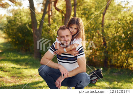 Little girl embracing her dad that is sitting in the forest. Having weekend in the woods Little girl embracing her dad that is sitting in the forest. Having weekend in the woods 125120174