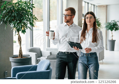 Holding tablet. Man and woman in formal clothes are working together indoors 125120266