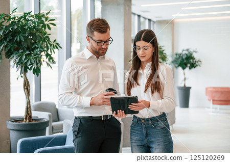 With tablet in hands. Man and woman in formal clothes are working together indoors 125120269