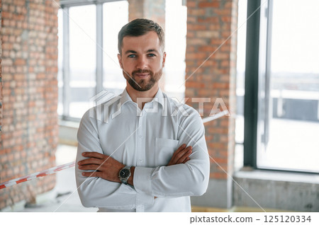 Standing with arms crossed. Man in white shirt is working indoors at construction site. Managing the project 125120334