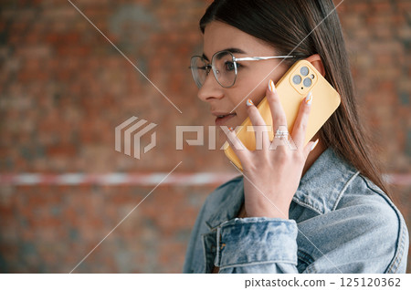 Talking by phone. Young woman is standing in the unfinished building on construction site and working on a project 125120362