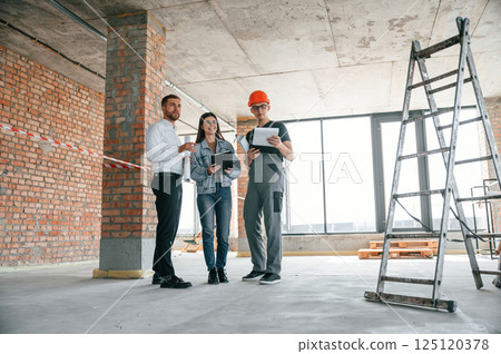 Male manager, foreman and woman is together on the construction site, talking about project Male manager, foreman and woman is together on the construction site, talking about project 125120378