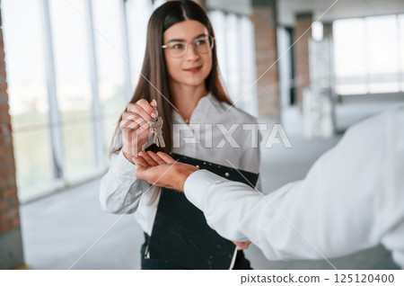 Receiving keys for her new home indoors. Happy young woman with a man 125120400