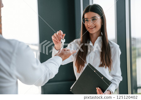 Receiving keys for her new home indoors. Happy young woman with a man 125120402