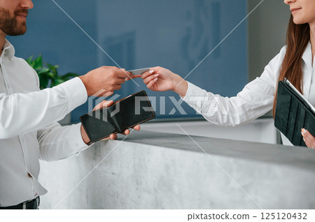 Taking keys at reception. Man in white shirt is ordering a room in the hotel by woman's help 125120432