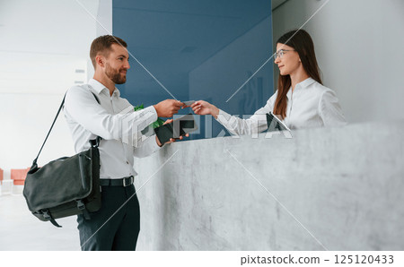 Assistant helping customer. Man in white shirt is ordering a room in the hotel by woman's help Assistant helping customer. Man in white shirt is ordering a room in the hotel by woman's help 125120433
