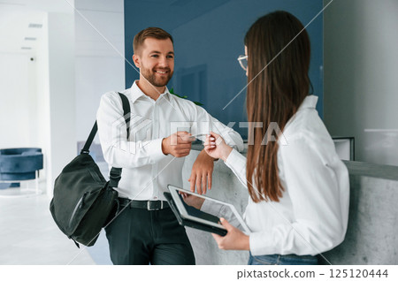 Man in white shirt is ordering a room in the hotel by woman's help 125120444