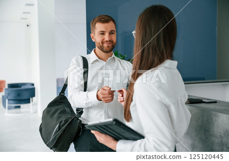 Man in white shirt is ordering a room in the hotel by woman's help 125120445
