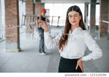 Man is working at background. Happy young woman is holding keys for the new apartment 125120500