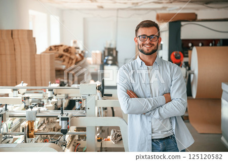 Handsome man is standing and smiling. Print house worker in white clothes is indoors Handsome man is standing and smiling. Print house worker in white clothes is indoors 125120582