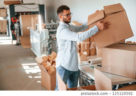 Moving the boxes with raw material. Print house worker in white clothes is indoors 125120592