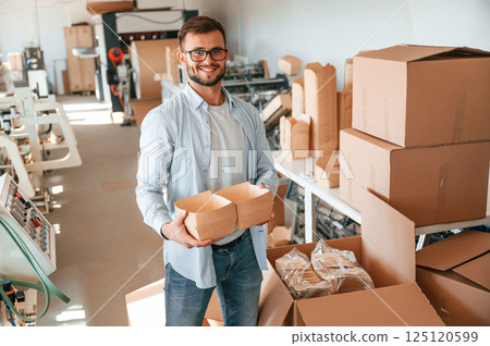 Holding beautiful wooden packages. Print house worker in white clothes is indoors Holding beautiful wooden packages. Print house worker in white clothes is indoors 125120599