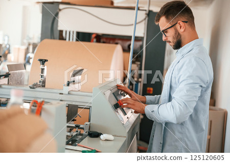 Operating printing cutting machine. Print house worker in white clothes is indoors Operating printing cutting machine. Print house worker in white clothes is indoors 125120605
