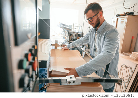 Working with wooden sheets. Man in print house that in white clothes is indoors Working with wooden sheets. Man in print house that in white clothes is indoors 125120615