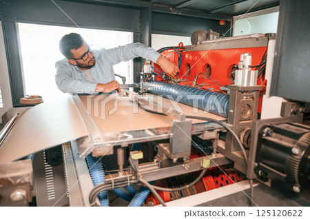 Sheet cutting machine. Operating device. Print house worker in white clothes is indoors 125120622