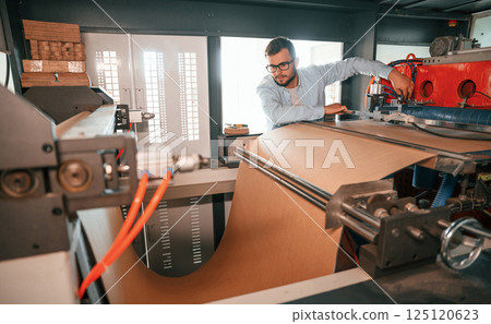 Sheet cutting machine. Operating device. Print house worker in white clothes is indoors 125120623