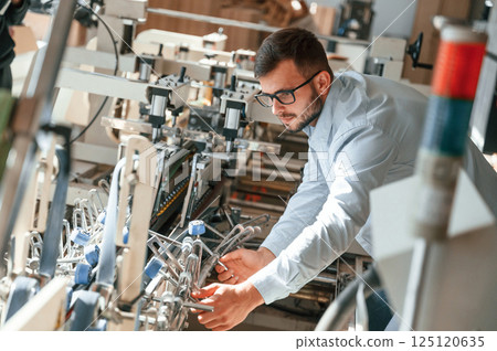 Setting up a printing machine. Typography worker in white clothes is indoors Setting up a printing machine. Typography worker in white clothes is indoors 125120635