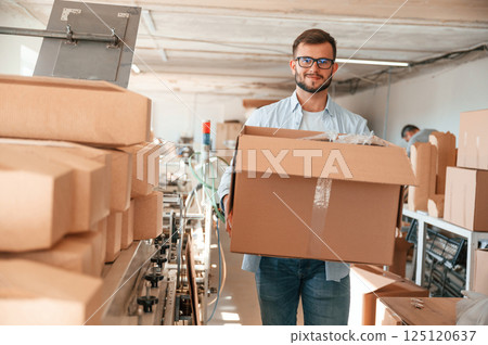 Moving the boxes with raw material. Print house worker in white clothes is indoors Moving the boxes with raw material. Print house worker in white clothes is indoors 125120637