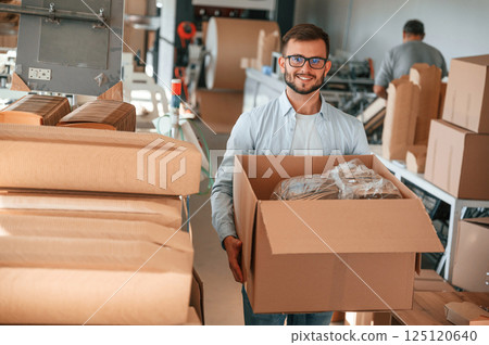 Moving the boxes with raw material. Print house worker in white clothes is indoors 125120640