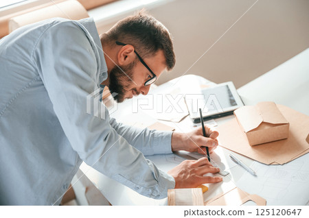 Doing measurements and drawing new design. Print house worker in white clothes is indoors 125120647