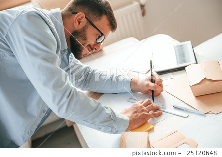 Doing measurements and drawing new design. Print house worker in white clothes is indoors Doing measurements and drawing new design. Print house worker in white clothes is indoors 125120648