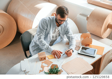 Sitting and working by the table. Print house employee in white clothes is indoors Sitting and working by the table. Print house employee in white clothes is indoors 125120658