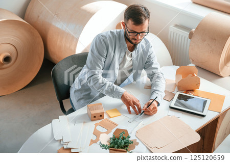 Sitting and working by the table. Print house employee in white clothes is indoors 125120659