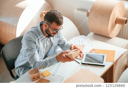 Sitting and working by the table. Print house employee in white clothes is indoors Sitting and working by the table. Print house employee in white clothes is indoors 125120660