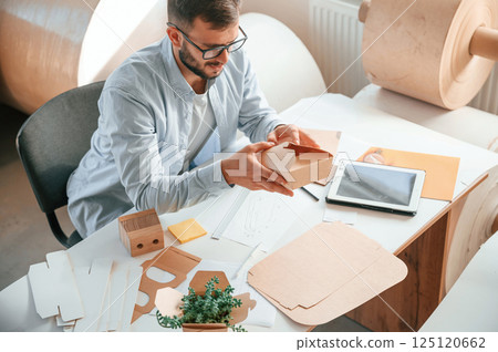 Sitting and working by the table. Print house employee in white clothes is indoors Sitting and working by the table. Print house employee in white clothes is indoors 125120662