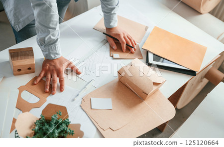 Standing by the table and looking at draws. Print house worker in white clothes is indoors Standing by the table and looking at draws. Print house worker in white clothes is indoors 125120664