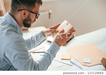 Holding little wooden box. Print house worker in white clothes is indoors 125120668
