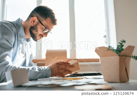 Holding little wooden box. Print house worker in white clothes is indoors 125120674