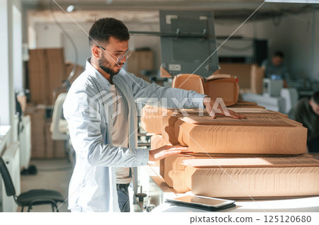 Print house worker in white clothes is indoors taking bunch of wooden sheets Print house worker in white clothes is indoors taking bunch of wooden sheets 125120680