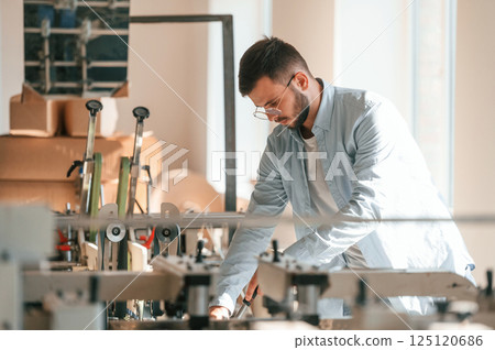 Modern printing machine. Typography worker in white clothes is indoors Modern printing machine. Typography worker in white clothes is indoors 125120686