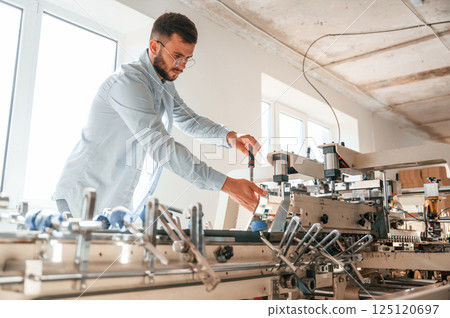 Setting up a printing machine. Typography worker in white clothes is indoors Setting up a printing machine. Typography worker in white clothes is indoors 125120697