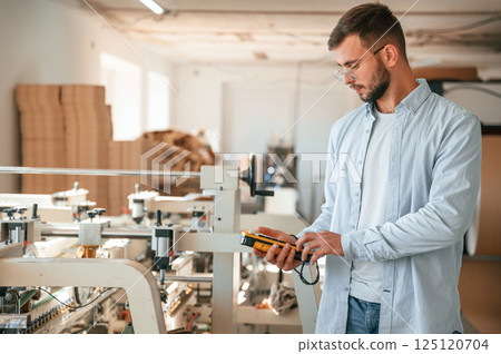 Holding controller of printing machine. Polygraph worker in white clothes is indoors Holding controller of printing machine. Polygraph worker in white clothes is indoors 125120704